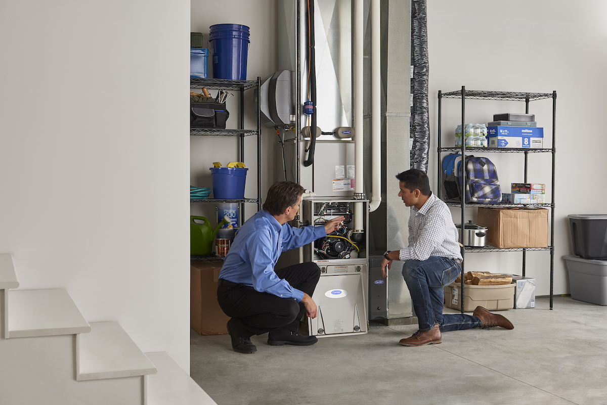 A Carrier dealer instructs a homeowner how to maintain and check their Carrier furnace in the basement